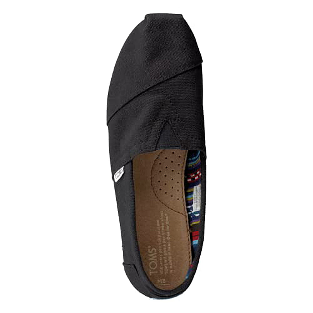 The TOMS Classic Canvas - Men is a black alpargata slip-on with a tan insole, patterned inner lining, and a small white logo tag on the side, shown from above.