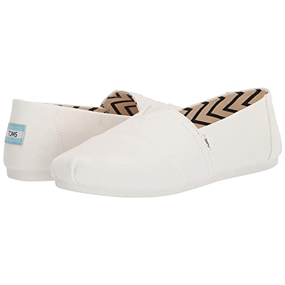 The TOMS Alpargata - Womens slip-on shoes feature a white canvas upper with subtle stitching, a chevron-patterned lining, recycled cotton material, and a blue-and-white TOMS label on the back heel.