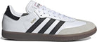 The adidas Samba OG - Men features a white leather upper with black stripes, suede toe cap, gold SAMBA text, gum rubber sole, white laces, and a black heel accent for a classic street style look.