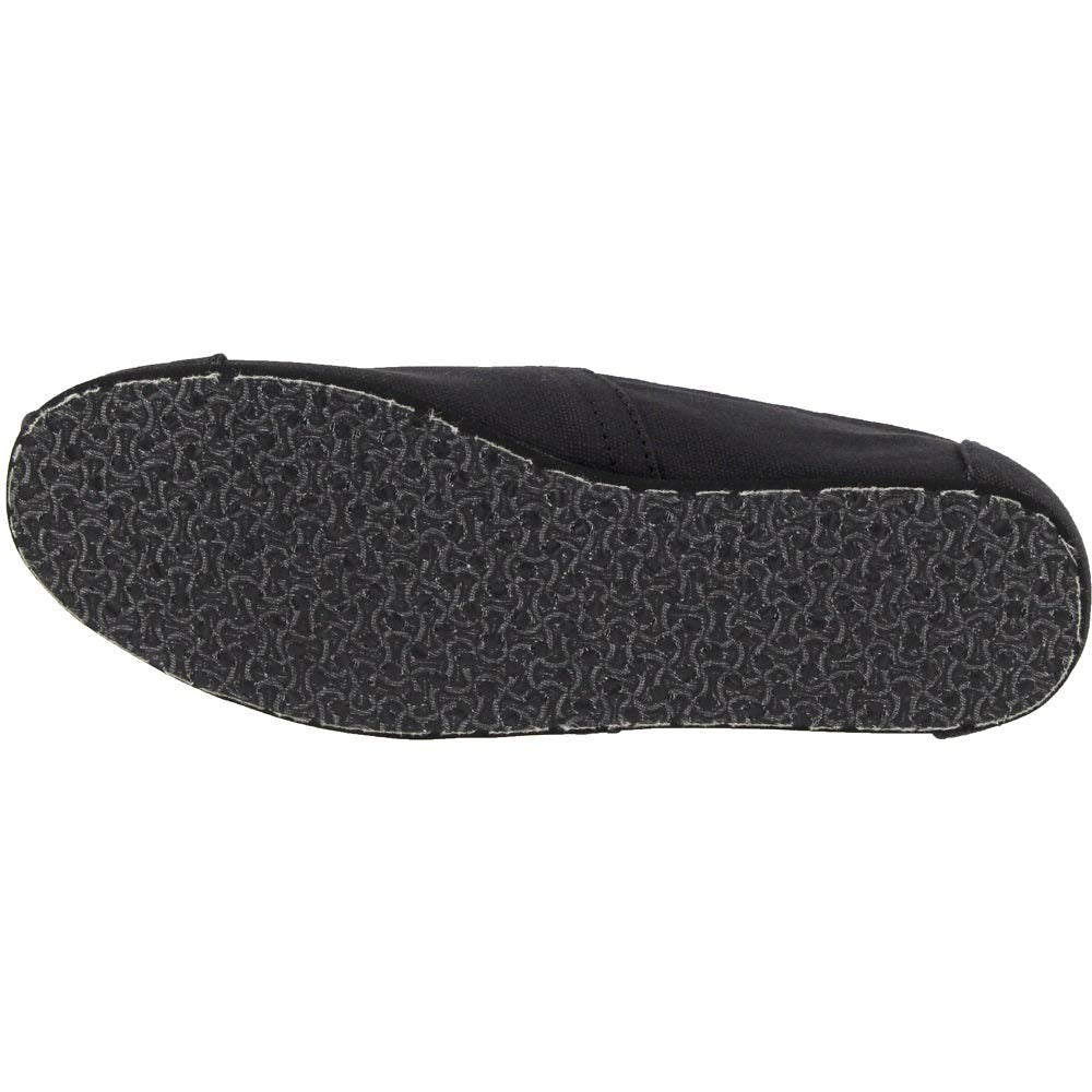 The image shows the bottom view of a TOMS Classic Canvas - Men slip-on, featuring a black upper and a textured, wavy-patterned rubber sole. This casual shoe offers comfortable everyday wear with its convenient design.