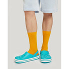 A person in bright yellow socks and light blue Crocs Crocband Clog Seasonal Colors - Unisex stands on a light surface, with only their legs and part of their shorts visible.