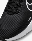 Close-up of the Nike Downshifter 12 - Women running shoe, showing textured black fabric, black laces, a white Nike swoosh logo, and a white midsole for lightweight support in a modern design.