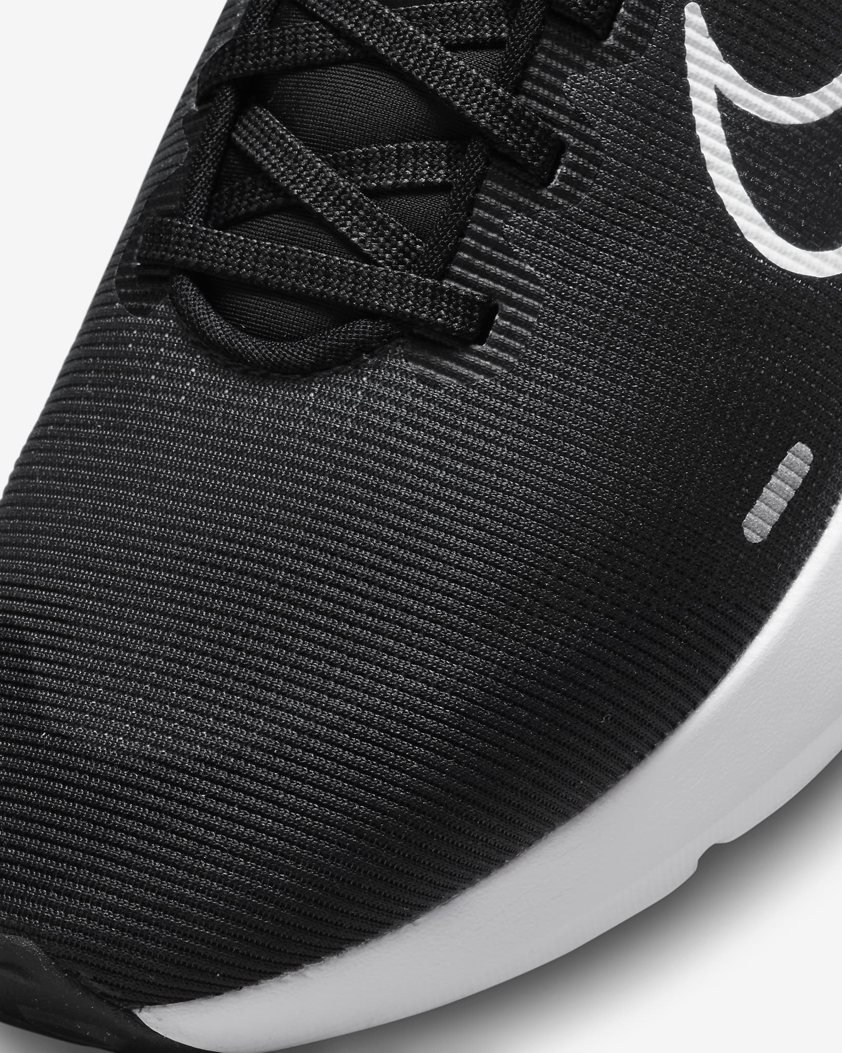 Close-up of the Nike Downshifter 12 - Women running shoe, showing textured black fabric, black laces, a white Nike swoosh logo, and a white midsole for lightweight support in a modern design.