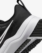 Close-up of the heel and side of the Nike Downshifter 12 - Women running shoe in black with a white sole and swoosh; textured fabric and tread highlight its lightweight support.