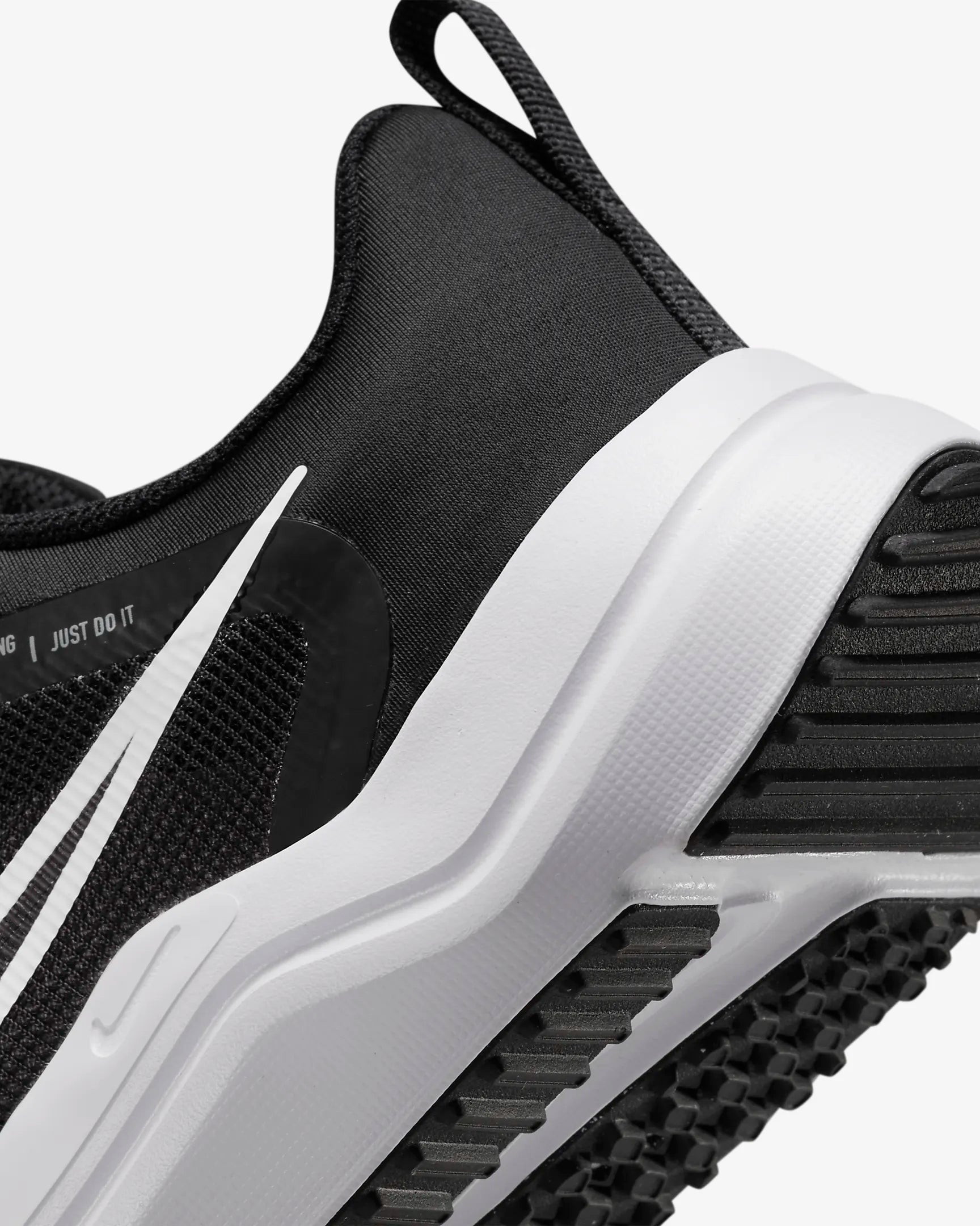 Close-up of the heel and side of the Nike Downshifter 12 - Women running shoe in black with a white sole and swoosh; textured fabric and tread highlight its lightweight support.