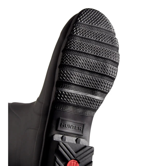 Close-up of the textured black rubber sole on Hunter Original Short Rain Boots - Women, featuring the embossed brand name near the heel and a red circular detail below it, set against a white background. Ideal for festivals and adventures.